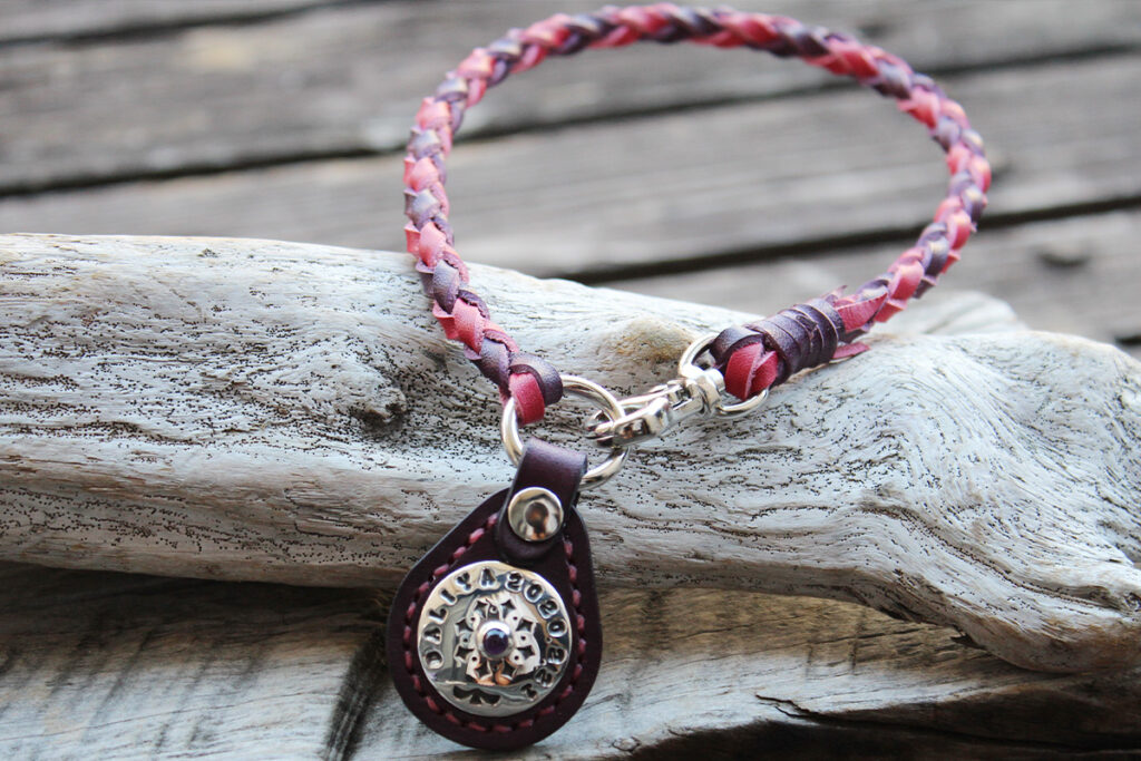 ビビットピンクと紫の編み込みネックレスタイプのネームタグ。タグ部分は紫革で、シルバーコンチョ（KOAアメジストの石）が飾られています。